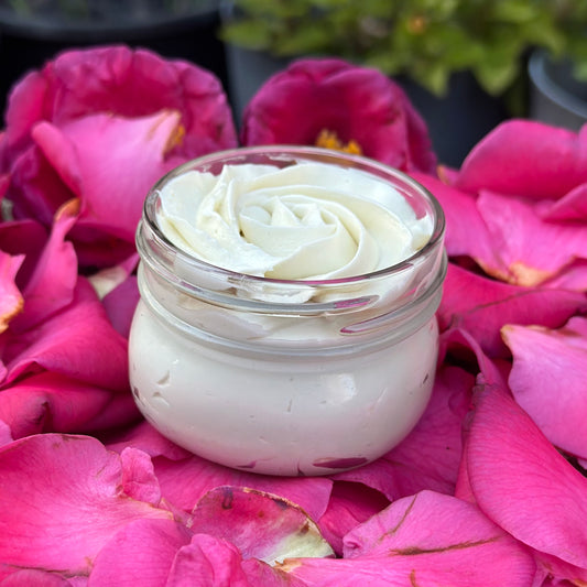 A jar of Romantic Rose Body Butter placed on a bed of pink rose petals, with a soft, moist texture visible outside the jar, revealing the beautiful rose design piped into the jar.