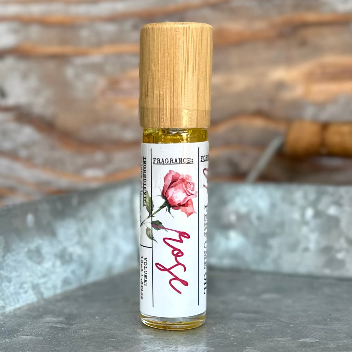 Roll-on bottle of rose perfume oil with bamboo cap and floral label on a metal tray