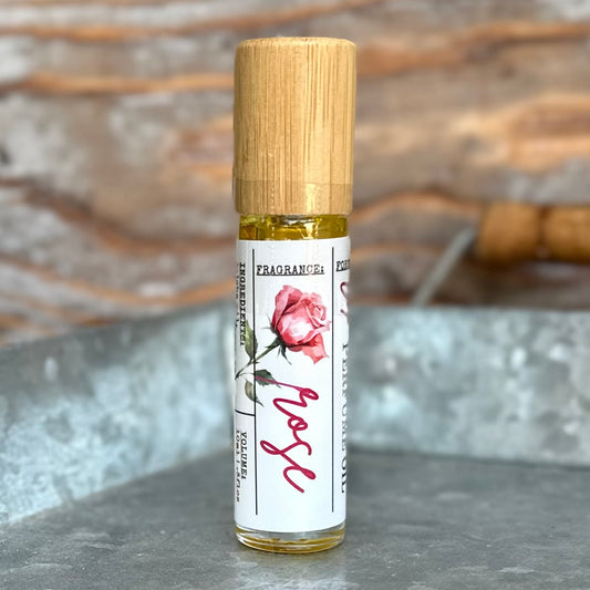 Roll-on bottle of rose perfume oil with bamboo cap and floral label on a metal tray