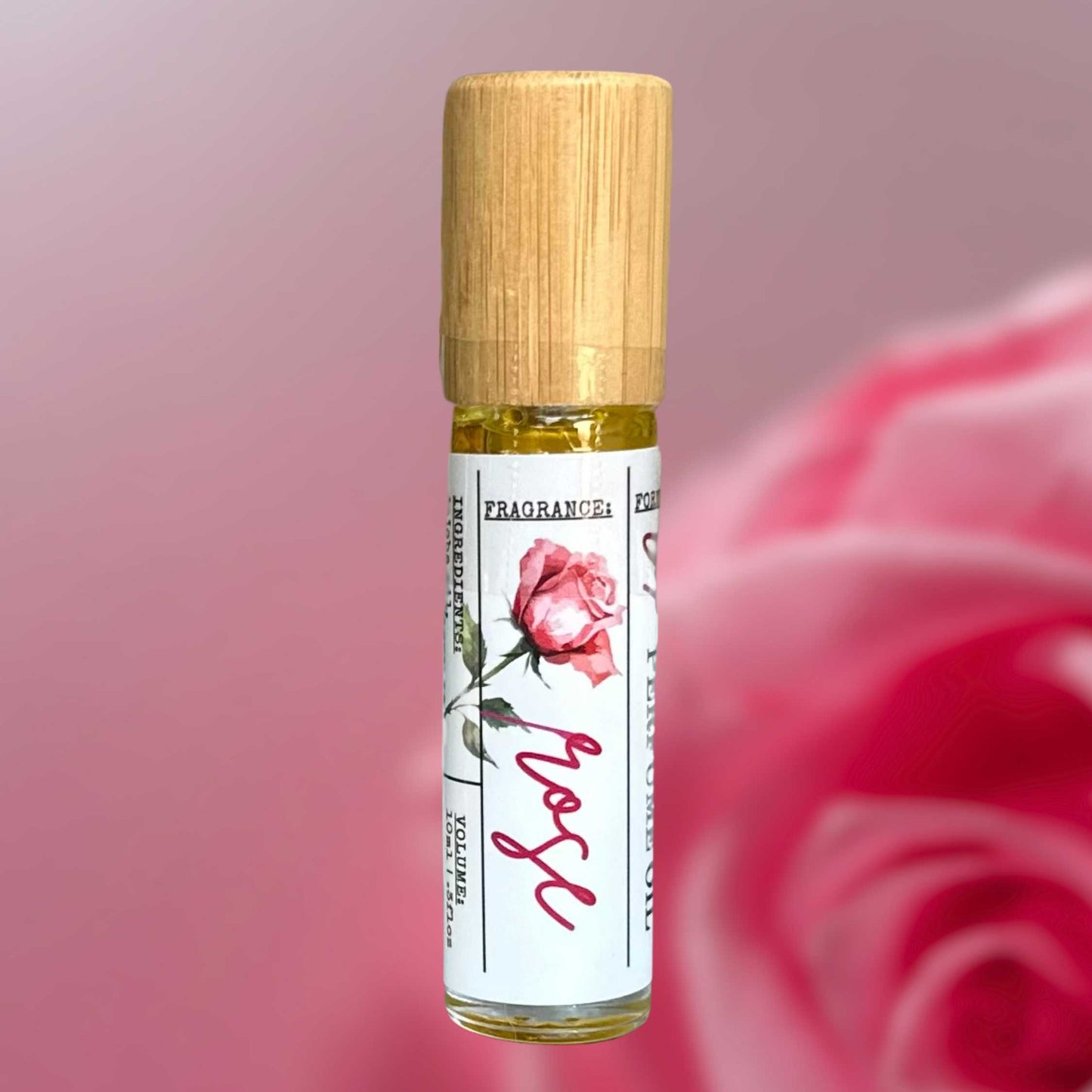 Roll-on perfume bottle with wooden cap and pink rose design on label against a blurred pink rose background