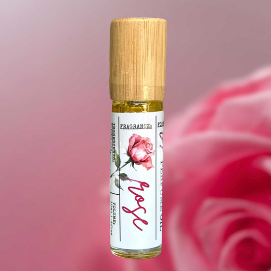 Roll-on perfume bottle with wooden cap and pink rose design on label against a blurred pink rose background