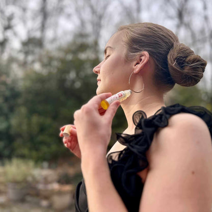 Woman applying perfume outdoors with trees in the background