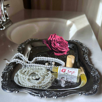 Tray with pearls, a bottle of rose perfume, and a pink rose on a sink.