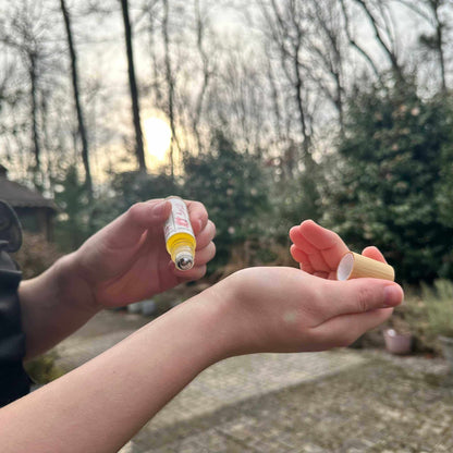 Two hands holding a small glass rollin outdoors with trees and sunlight in the background.