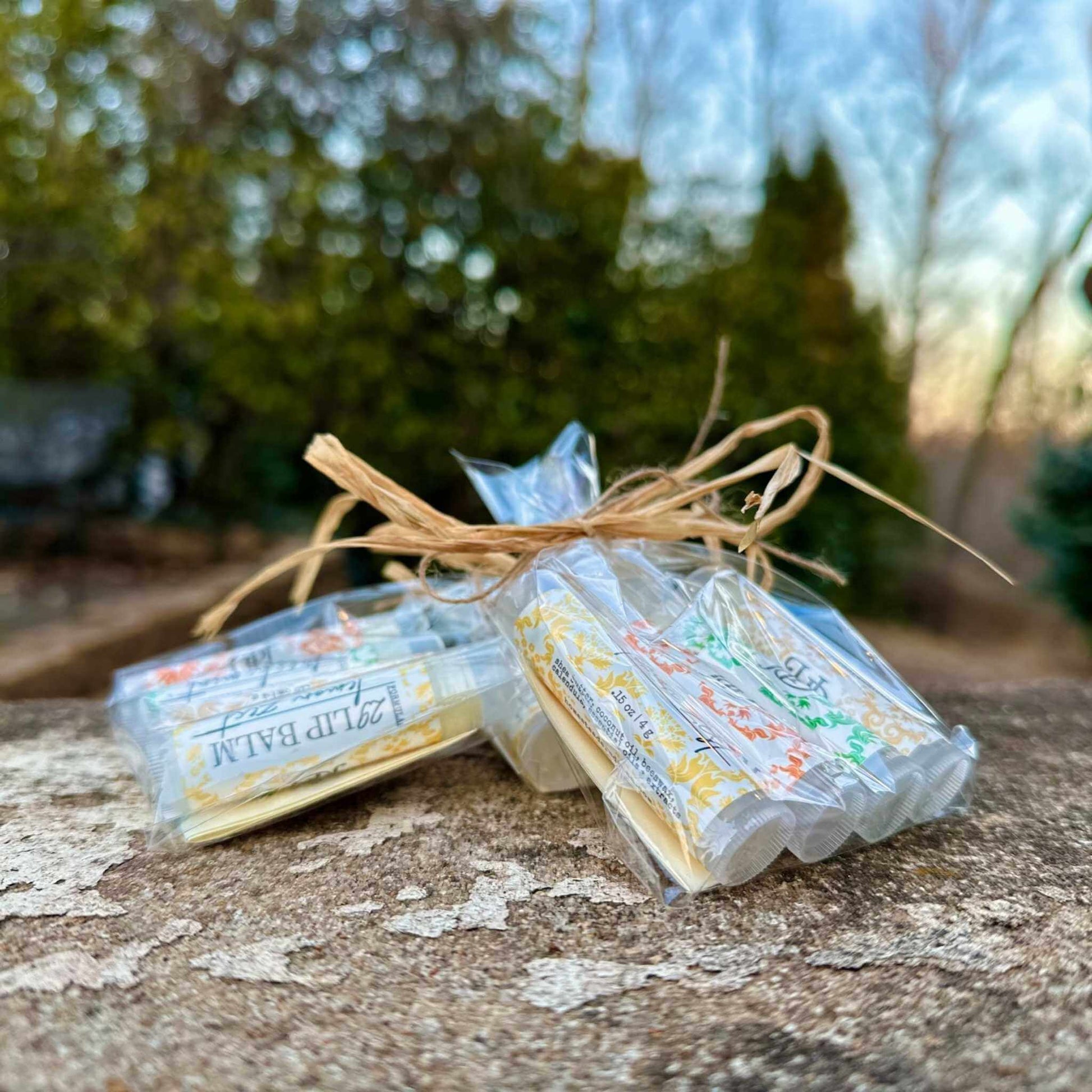 Three wrapped lip balm sets tied with twine on a stone surface with a blurred natural background