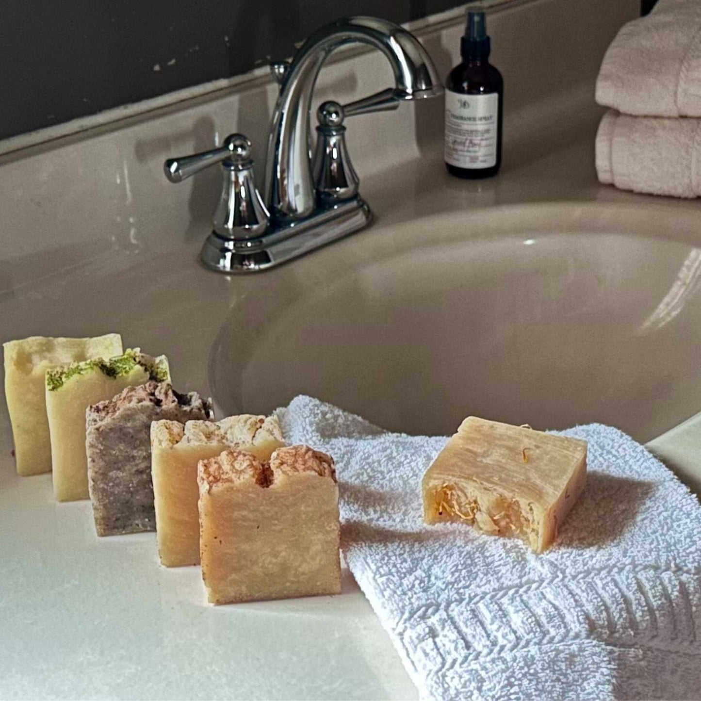 Various soap bars on a towel in front of a sink with a bottle and towel in the background.
