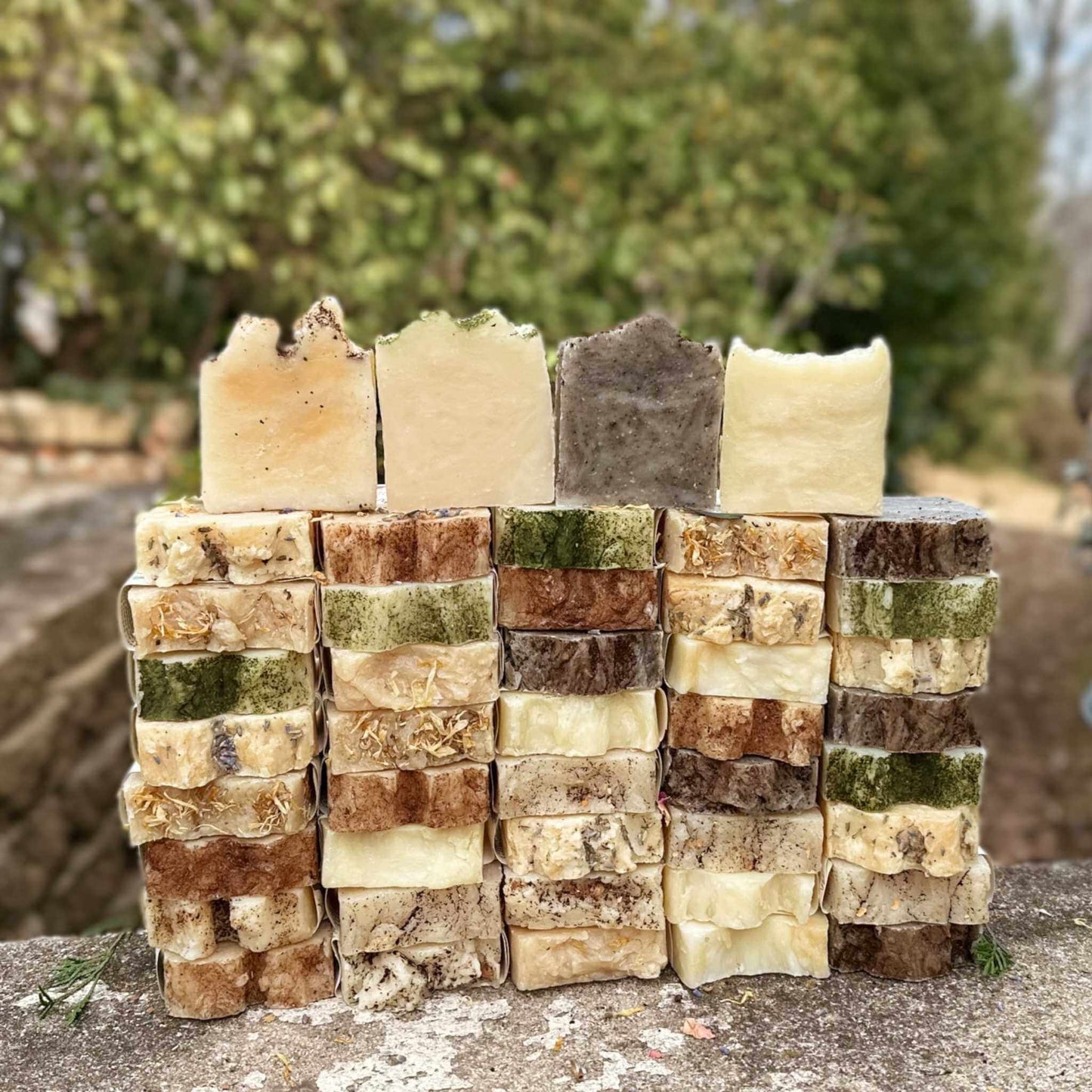 Stack of variously colored soap bars on a stone surface with a blurred natural background