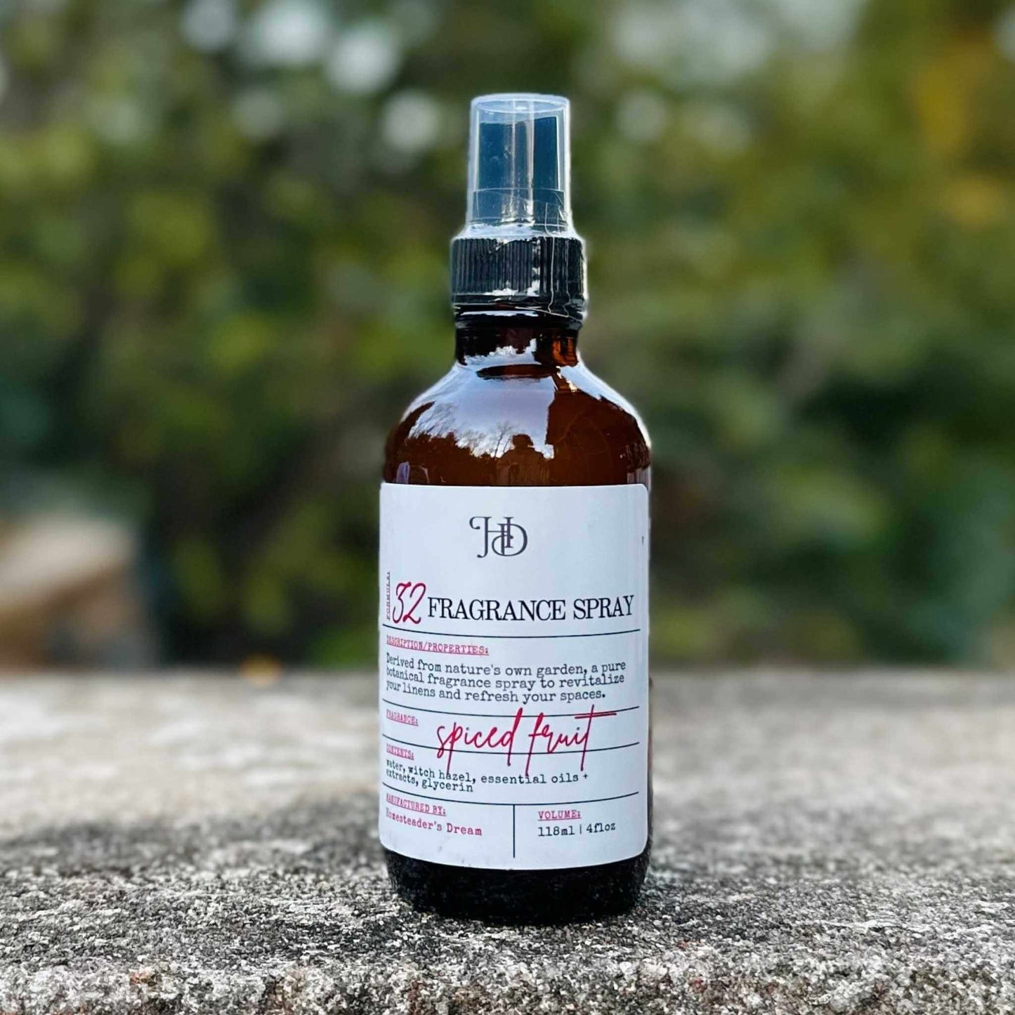 Fragrance spray bottle labeled 'Spiced Fruit' on a stone surface with a blurred green background