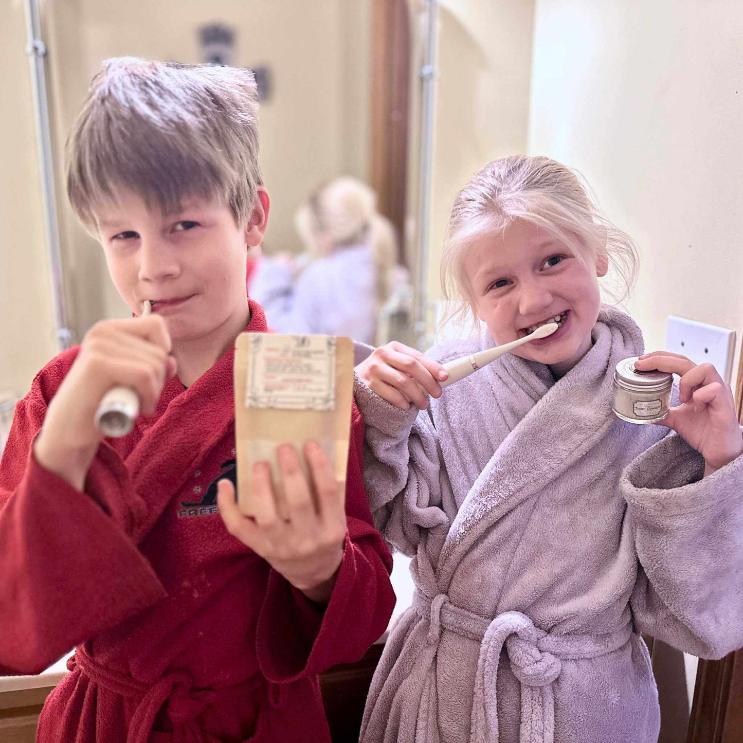 Two children in bathrobes brushing their teeth in a bathroom.