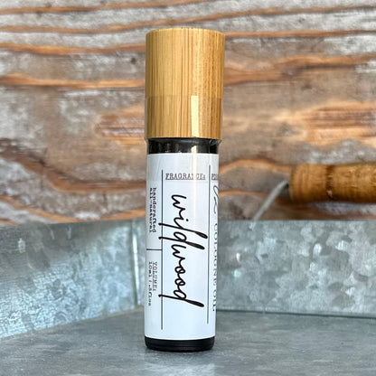 Roll-on bottle of wildwood cologne oil with bamboo cap on a rustic background