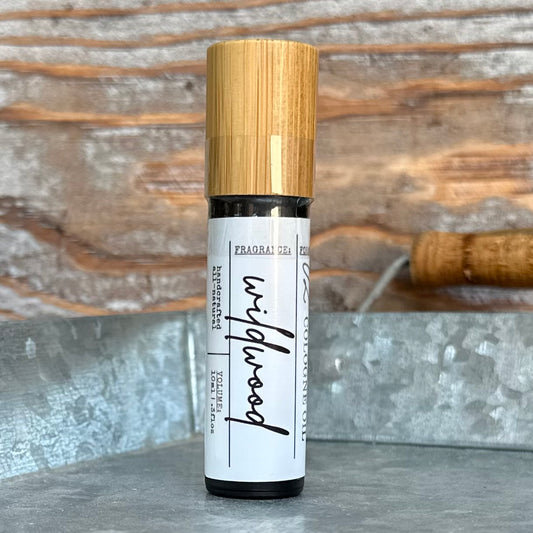 Roll-on bottle of wildwood cologne oil with bamboo cap on a rustic background