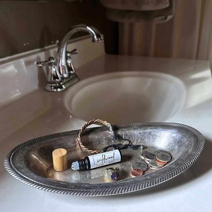 Silver tray with personal items including a roll-on bottle, wooden lid, and coins on a bathroom sink.