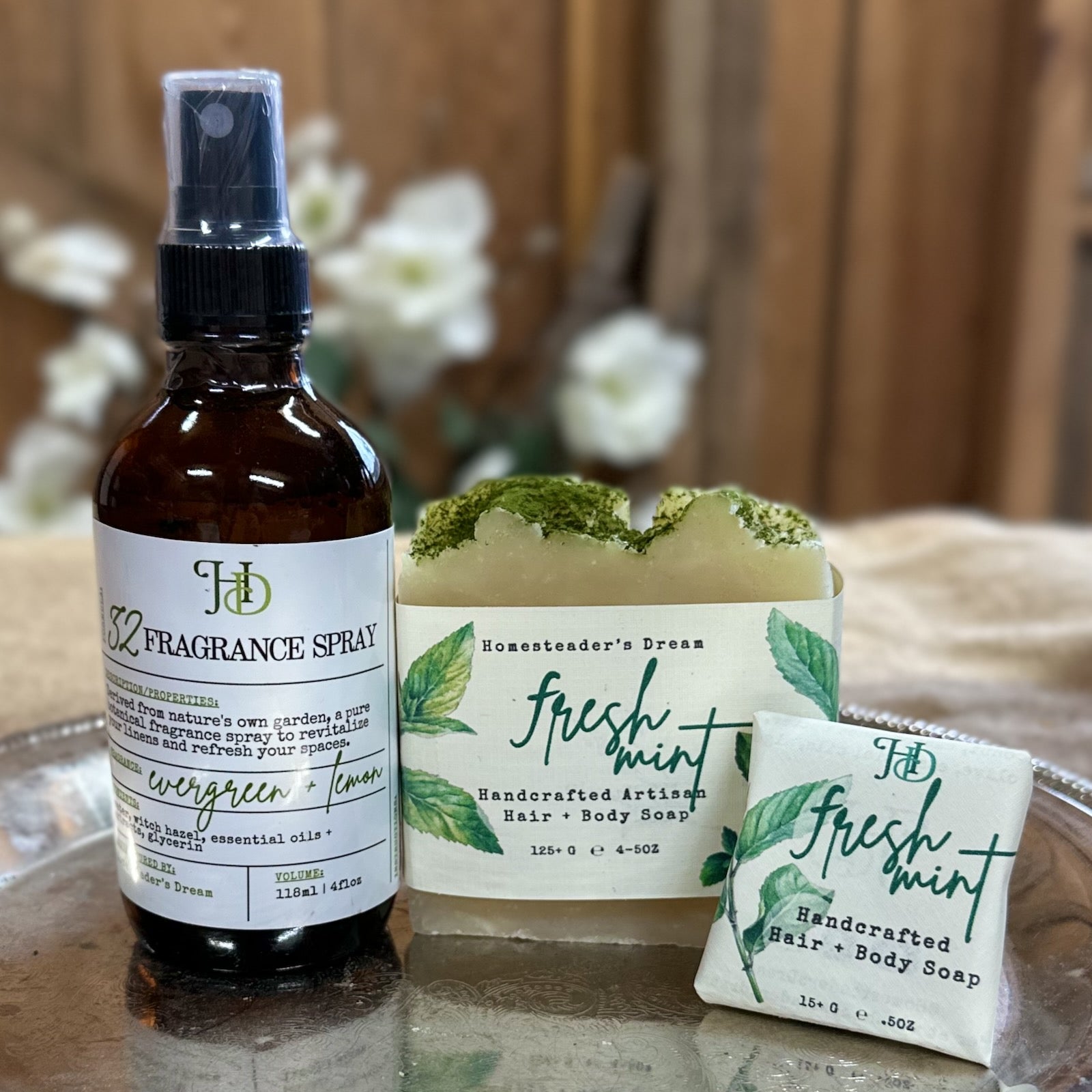 Bottle of evergreen and lemon fragrance spray and two bars of fresh mint soap on a silver tray with a wooden background.